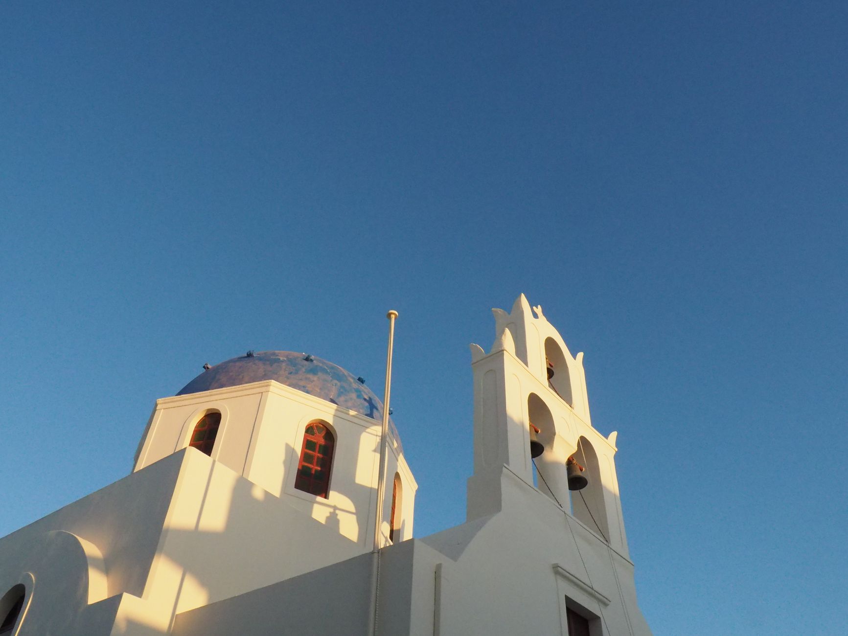 Low angle view of a traditional white church with blue dome in Santorini against a clear sky.